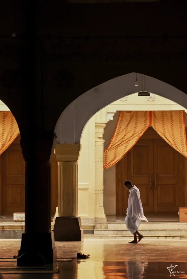 A lone figure walking past a lit arched doorway