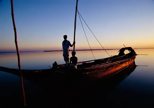 Two men on a wooden boat on the river at dusk