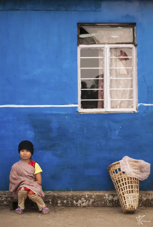 A child sitting beside a basket against a bright blue wall