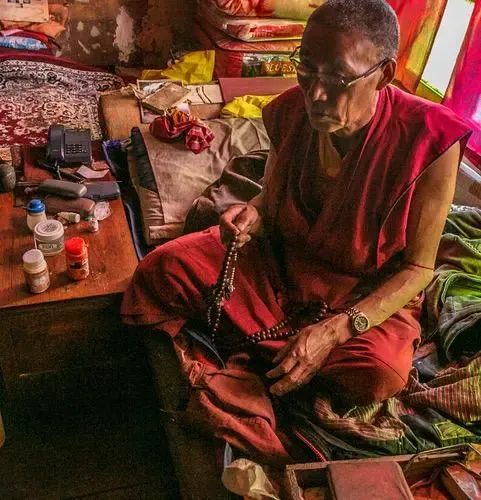 A figure in maroon robes seated among colourful wares