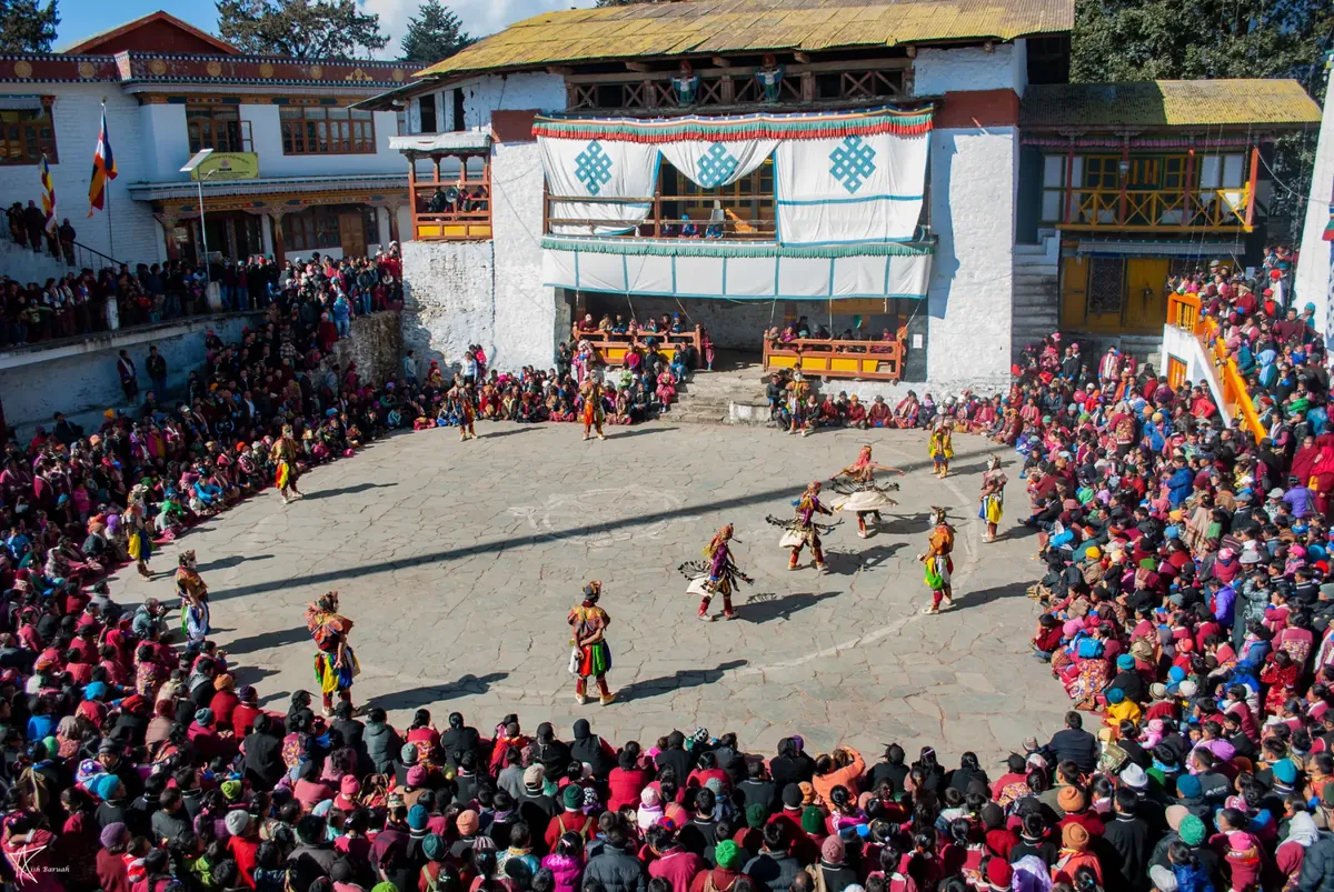 Crowds watch masked dancers in the courtyard of a Buddhist monastery during a festival