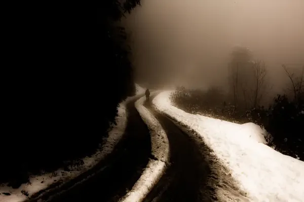 A snowy mountain road disappearing into mist as darkness falls