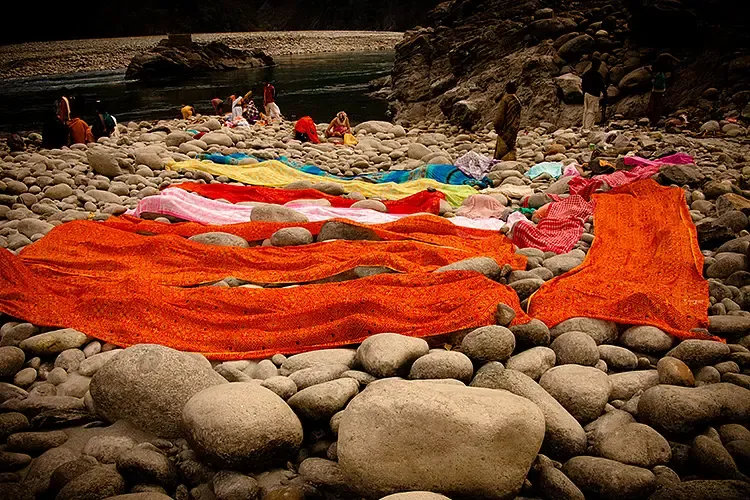 Brightly coloured cloths laid out to dry on river stones at Parasuram Kund