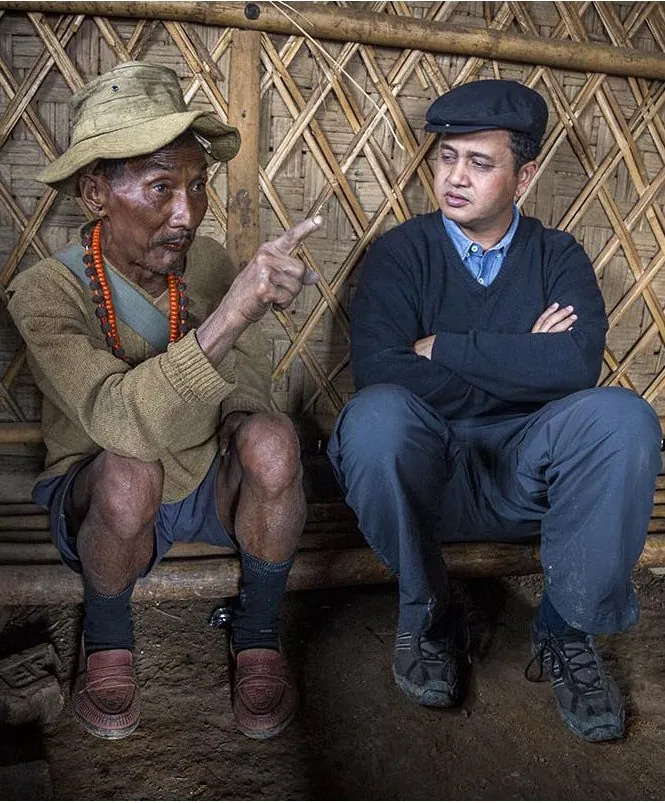 Rajan Dowerah sitting with an elder inside a bamboo house