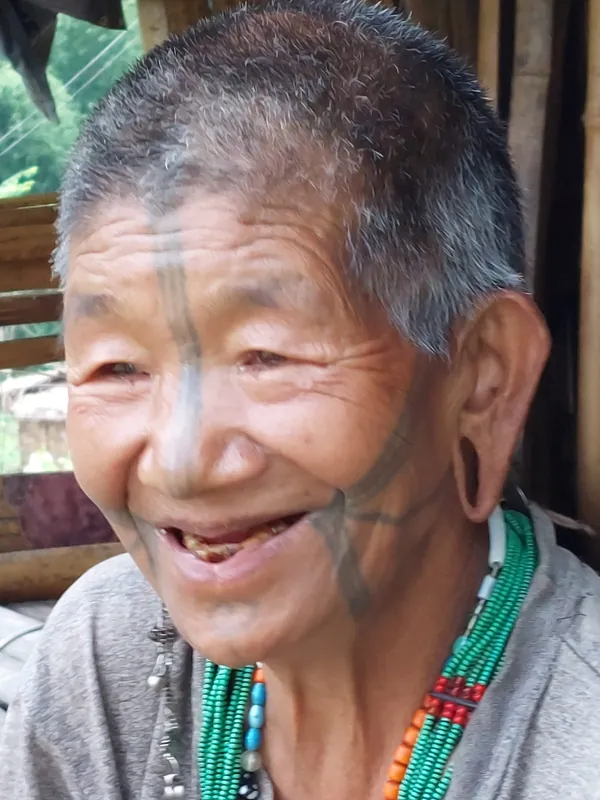 A smiling elder with facial tattoos and ear ornaments