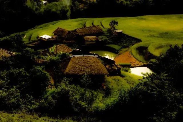 Thatched village houses glowing on a green hillside at dusk